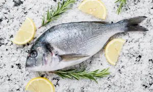 Orata al sale, pronta per essere cucinata, adagiata su un letto di sale grosso con spicchi di limone e rametti di rosmarino.