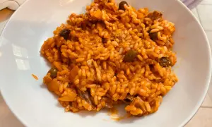 Un invitante risotto al pomodoro, ricco e saporito, con pezzetti di carne e olive nere, servito in una ciotola bianca.