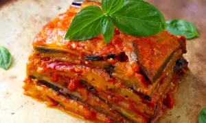 Una fetta di parmigiana di melanzane ricetta originale, stratificata e succulenta, guarnita con basilico fresco.