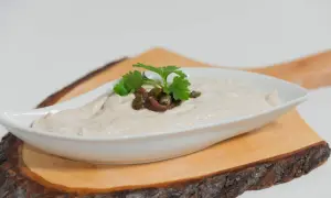 Salsa tonnata cremosa, guarnita con acciughe, capperi e prezzemolo, servita in una ciotola bianca su un tagliere di legno.
