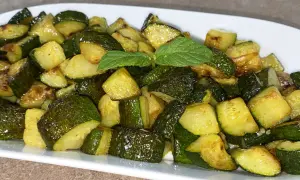 Un piatto di zucchine trifolate, tagliate a cubetti e cotte fino a doratura, guarnite con una fogliolina di menta.