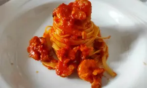 Un nido di pasta fresca avvolto in un ricco sugo di pesce, con gamberi succulenti che si adagiano sul piatto bianco.
