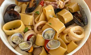 Un piatto invitante di calamarata allo scoglio, con pasta grossa, cozze, vongole e anelli di calamaro, condito con pomodorini e prezzemolo.
