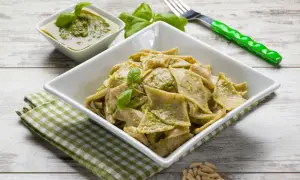 Testaroli ricetta: pasta fresca condita con pesto alla genovese, guarnita con basilico e pinoli.