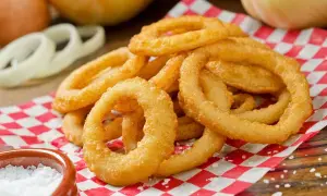 Anelli di cipolla dorati e croccanti, perfetti per capire come si fa la pastella. Serviti su carta a quadri rossi con sale grosso.