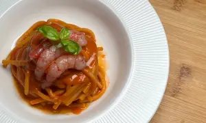 Spaghetti conditi con un sugo rosso intenso, guarniti con gamberi rosa e basilico fresco. Un piatto che evoca il sapore del mare, come una ricca bisque di crostacei.