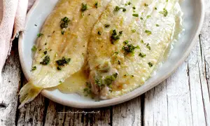 Sogliola alla mugnaia dorata e succulenta, cosparsa di prezzemolo fresco, servita su un piatto ovale.