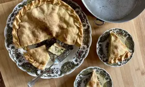 Una torta di riso e zucchine alla ligure, dorata e invitante, servita su un piatto decorato. Due fette sono già state tagliate, pronte per essere gustate.
