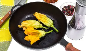 Fiori di zucca in padella, pronti per essere impanati e fritti. Accanto, spezie e un macina sale.