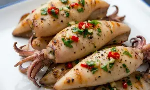Calamari alla piastra succulenti, conditi con aglio, peperoncino e prezzemolo fresco, serviti su un piatto bianco.