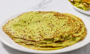 Piatto di crepes di zucchine verdi, sottili e leggermente dorate, impilate su un piatto bianco.