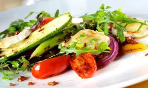 Deliziosi contorni estivi: zucchine grigliate, pomodorini, cipolla rossa e formaggio di capra su un letto di rucola.