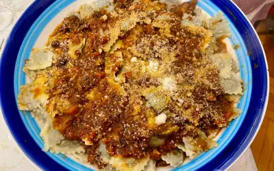 Piatto di ravioli alla genovese con sugo ricco e abbondante parmigiano grattugiato, serviti in un piatto blu e bianco.