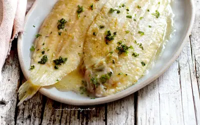 Sogliola alla mugnaia dorata e succulenta, cosparsa di prezzemolo fresco, servita su un piatto ovale.