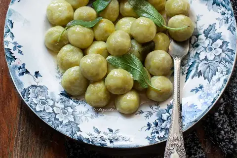 Piatto di gnocchi di zucchine fatti in casa, conditi con burro e salvia, su un piatto decorato con fiori blu.