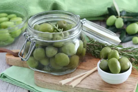 Verdi olive in salamoia per olive, conservate in un barattolo di vetro con rametti di rosmarino.