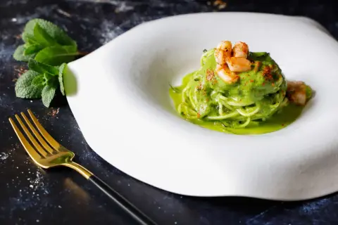 Spaghetti di zucchine con gamberi e salsa verde, guarniti con paprika e menta fresca. Un piatto leggero e colorato.