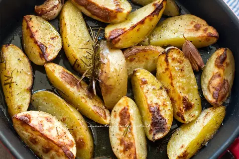 Patate con la buccia dorate al forno, condite con rosmarino e aglio. Un contorno rustico e saporito.