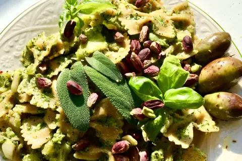 Farfalle condite con un saporito pesto di salvia, guarnite con pistacchi, basilico e olive verdi.