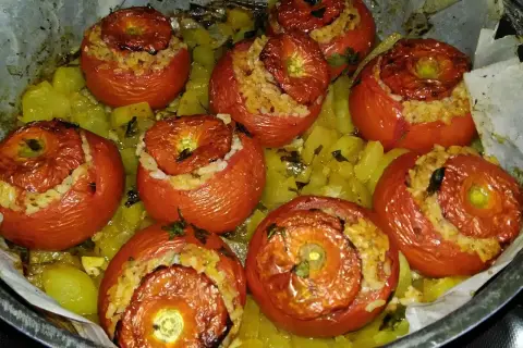 Pomodori ripieni di riso, cotti al forno su un letto di patate e erbe aromatiche. Un piatto saporito e colorato.