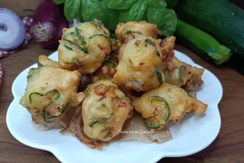 Frittelle di zucchine dorate e croccanti, pronte per essere gustate. Sullo sfondo, ingredienti freschi come basilico e cipolle rosse.