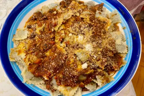 Piatto di ravioli alla genovese con sugo ricco e abbondante parmigiano grattugiato, serviti in un piatto blu e bianco.