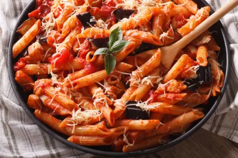 Piatto invitante di pasta con melanzane e pomodorini, condita con formaggio grattugiato e basilico fresco.