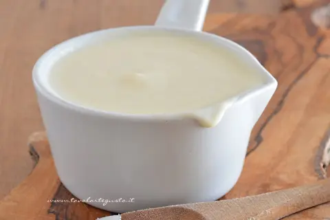 Una cremosa besciamella pronta per la tua ricetta, servita in una ciotolina bianca su un tagliere di legno.