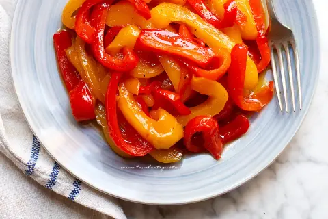Peperoni in agrodolce, un contorno colorato e saporito, servito su un piatto azzurro con forchetta.