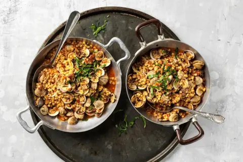 Due padelle piene di fregola con vongole, un piatto sardo profumato, guarnito con prezzemolo fresco.