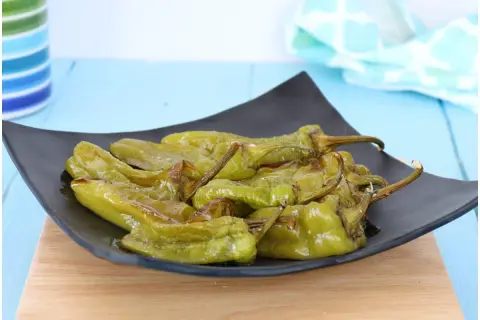 Friggitelli al forno, verdi e lucidi, serviti su un piatto nero. Un contorno saporito e facile da preparare.