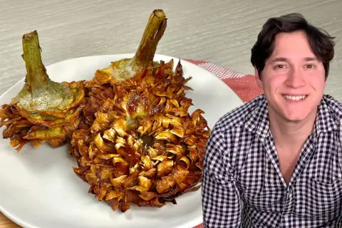 Due carciofi alla giudia dorati e croccanti su un piatto bianco, accanto a un uomo sorridente.