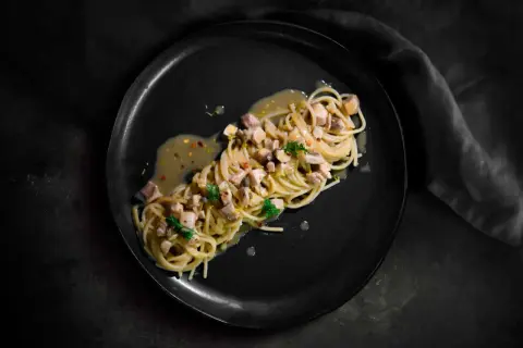 Spaghetti con ricciola, limone e peperoncino su piatto nero. Un piatto elegante e saporito.