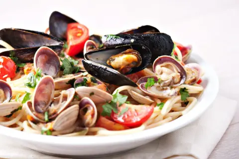 Un piatto invitante di tagliolini ai frutti di mare, con cozze, vongole e pomodorini freschi, guarnito con prezzemolo.