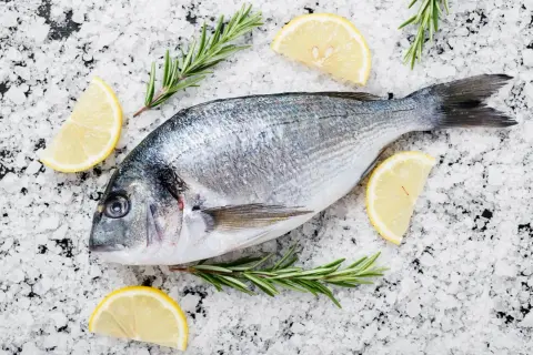 Orata al sale, pronta per essere cucinata, adagiata su un letto di sale grosso con spicchi di limone e rametti di rosmarino.