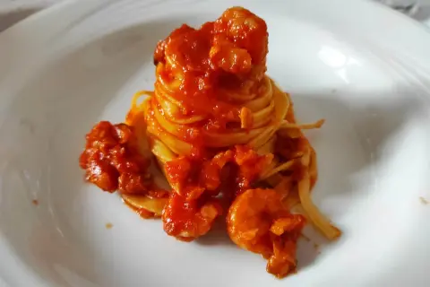 Un nido di pasta fresca avvolto in un ricco sugo di pesce, con gamberi succulenti che si adagiano sul piatto bianco.