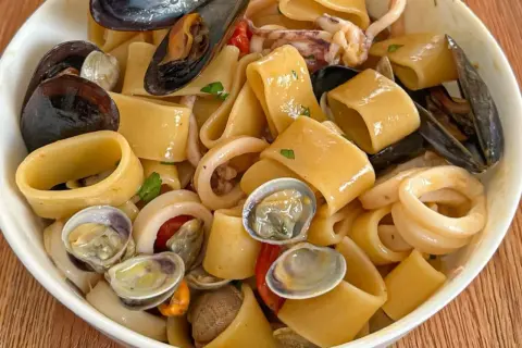 Un piatto invitante di calamarata allo scoglio, con pasta grossa, cozze, vongole e anelli di calamaro, condito con pomodorini e prezzemolo.