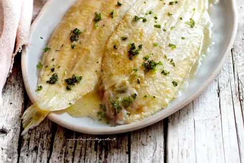 Sogliola alla mugnaia dorata e succulenta, cosparsa di prezzemolo fresco, servita su un piatto ovale.