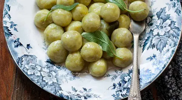 Piatto di gnocchi di zucchine fatti in casa, conditi con burro e salvia, su un piatto decorato con fiori blu.