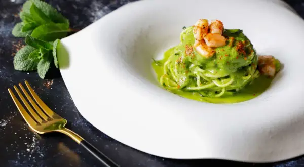 Spaghetti di zucchine con gamberi e salsa verde, guarniti con paprika e menta fresca. Un piatto leggero e colorato.