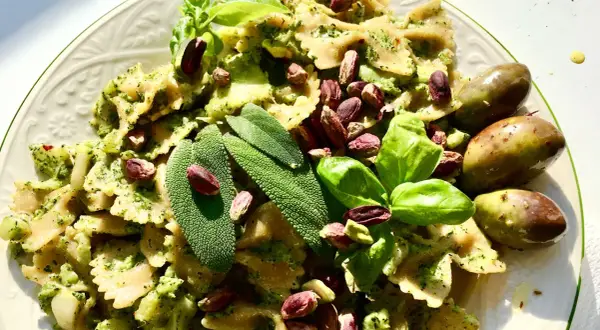 Farfalle condite con un saporito pesto di salvia, guarnite con pistacchi, basilico e olive verdi.
