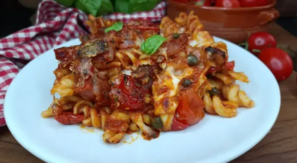 Piatto di pasta con pomodori al forno alla pugliese, filante e saporita, guarnita con basilico fresco.