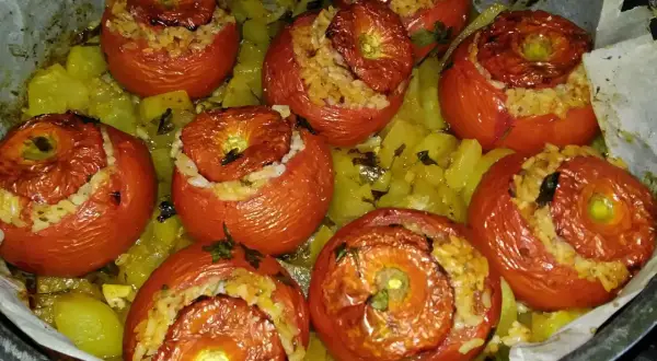 Pomodori ripieni di riso, cotti al forno su un letto di patate e erbe aromatiche. Un piatto saporito e colorato.