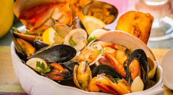 Un invitante piatto di zuppa di crostacei, ricco di cozze, vongole e gamberi, guarnito con limone e pane tostato.