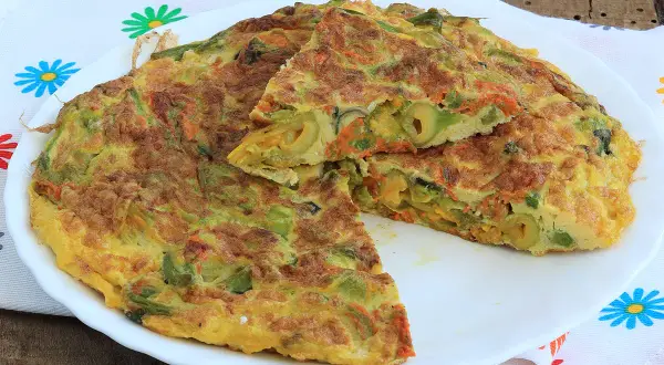 Frittata con fiori di zucca, carote e olive, tagliata a spicchi su un piatto bianco, con un tovagliolo colorato sullo sfondo.