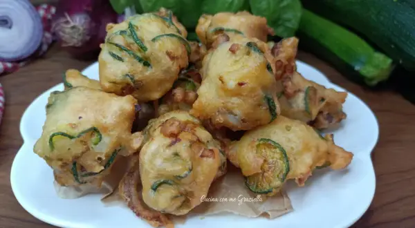 Frittelle di zucchine dorate e croccanti, pronte per essere gustate. Sullo sfondo, ingredienti freschi come basilico e cipolle rosse.