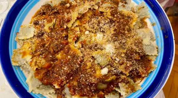 Piatto di ravioli alla genovese con sugo ricco e abbondante parmigiano grattugiato, serviti in un piatto blu e bianco.