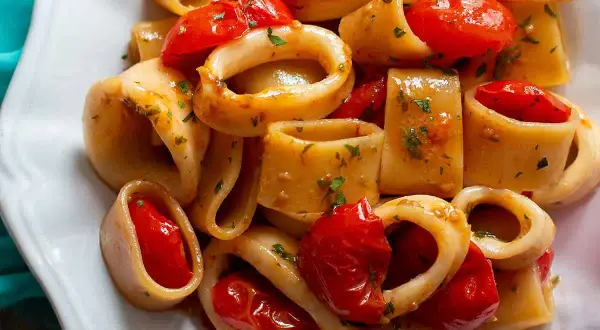 Piatto di calamarata ricetta originale con calamari e pomodorini freschi, guarnito con prezzemolo tritato.