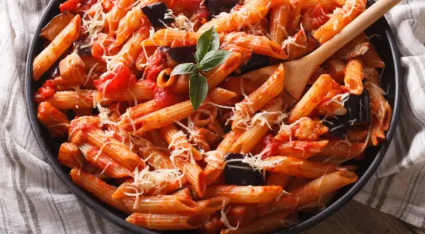 Piatto invitante di pasta con melanzane e pomodorini, condita con formaggio grattugiato e basilico fresco.