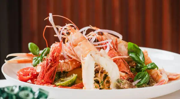 Un'appetitosa catalana di crostacei, con scampi, gamberi, pomodorini e basilico fresco, servita su un piatto bianco.